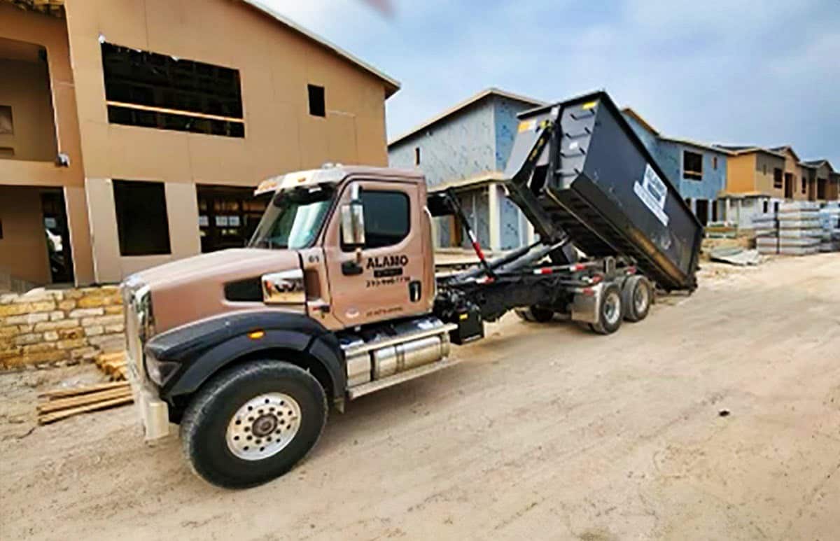 Alamo Disposal truck unloading a roll-off dumpster at a construction site